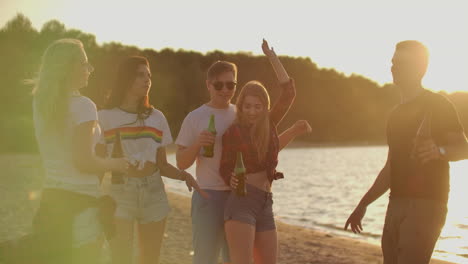 Group-of-students-celebrate-the-end-of-the-semester-with-beer-on-the-sand-beach.-They-are-dancing-on-the-open-air-party-at-sunset.
